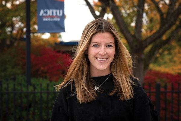 Jackie Rueckert stands in front of Utica College banner.